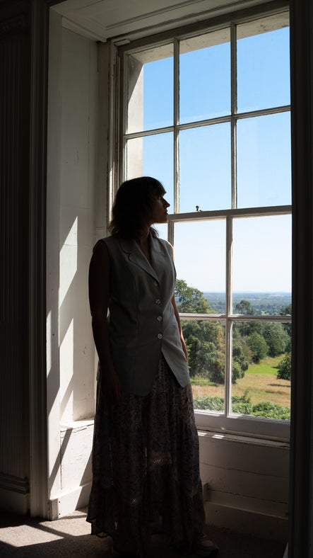 Woman standing, looking through the full length window at Leith Hill Place, as the sun streams in.